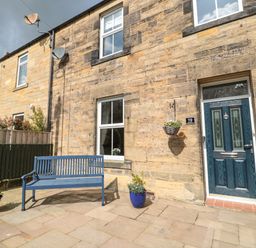 A blue bench and two flower pots outside a stone house with a blue door at 19 Duke Street in Alnwick