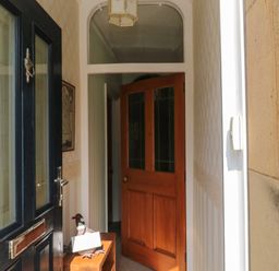 An open black front door showing a hallway with a wooden door and a small wooden bench with a decorative bird at 19 Duke Street in Alnwick
