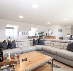 A living room with a grey sectional sofa black pillows wooden coffee table and dining area in the background at Penthouse 23 in Newquay