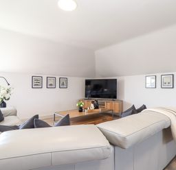 A living room with gray sofas a wooden coffee table a TV on a wooden stand wall art and a floor lamp at Penthouse 23 in Newquay