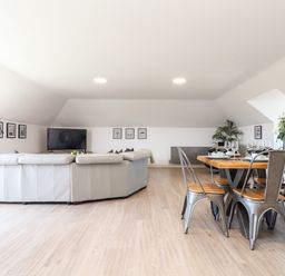 A living area with a large white sectional sofa a dining table with metal chairs and a television on a stand at Penthouse 23 in Newquay