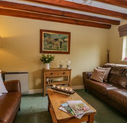 A living room with brown leather sofas a wooden coffee table with magazines a side table with candles and a painting on the wall at Columbine Cottage in Hawkshead