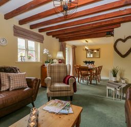 A living room with wooden beams on ceiling leather couches and a beige armchair next to a dining area with wooden chairs at Columbine Cottage in Hawkshead