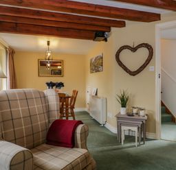 A living room with a plaid armchair a red blanket wooden beams a dining table with chairs and a heart-shaped wall decoration at Columbine Cottage in Hawkshead