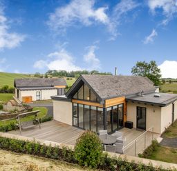 A modern house with a wooden deck patio and outdoor seating in a rural area at Forget Me Not Lodge in Bamburgh