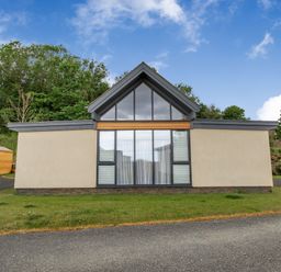 A modern single-story house with a large glass window and a triangular roof at Forget Me Not Lodge Bamburgh