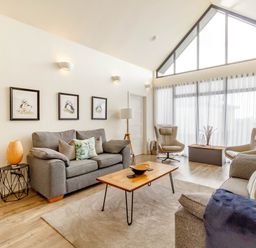 A living room with two gray sofas a wooden coffee table two beige armchairs and three framed pictures on the wall at Forget Me Not Lodge in Bamburgh