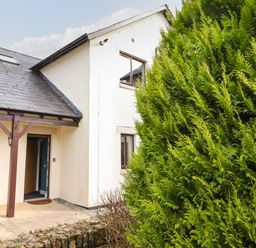An entrance to a beige house with a brown roof and a large green bush in front at Tilly Mint Cottage Nr Ullswater