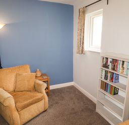 A small sitting area with an armchair next to a floor lamp and side table with a vase and a white bookshelf with books by a window at Tilly Mint Cottage Nr Ullswater