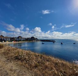 A coastal scene with houses along the shore boats on the water and grassy land in the foreground at Chesil Retreat in Weymouth