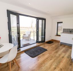 A kitchen with wooden floor a small round table with chairs flowers on the table and open patio doors leading outside at The Annexe in Llanfairpwllgwyngyll