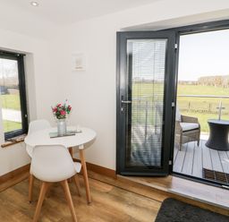 A dining area with a round white table and two white chairs next to a glass door opening to a patio with wicker chairs and a small table at The Annexe in Llanfairpwllgwyngyll