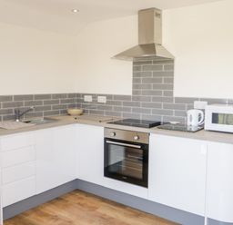 A kitchen with white cabinets a built in oven a stovetop a microwave a kettle a sink and gray tiled backsplash at The Annexe in Llanfairpwllgwyngyll