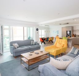 A living room with blue sofas a yellow armchair and a wooden coffee table next to a dining area with colorful chairs at 30 Cliff Edge in Newquay