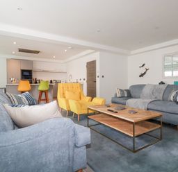A living room with blue sofas yellow armchairs a wooden coffee table and colorful bar stools at 30 Cliff Edge in Newquay