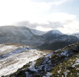 A snowy mountain landscape with rugged hills and a few people walking on a path at Nook Cottage in Rosthwaite near Keswick