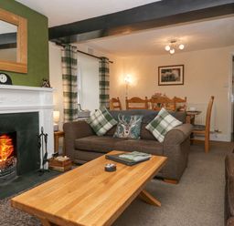 A living room with a fireplace two sofas a wooden coffee table and a dining table in the background at Nook Cottage in Rosthwaite near Keswick