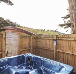 An outdoor blue hot tub next to a wooden fence with trees and a small wooden shed visible at 11 Towan Valley in Porthtowan