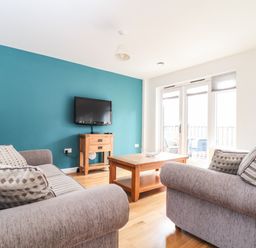 A living room with two gray sofas, a wooden coffee table, a wall-mounted TV, and glass doors leading to a balcony at 11 Towan Valley Porthtowan