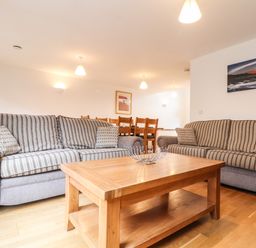 A living room with two striped sofas a wooden coffee table and a dining table with chairs at 11 Towan Valley in Porthtowan