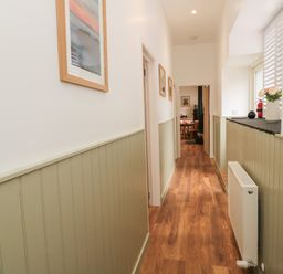 A hallway with wooden flooring and framed pictures on walls with green paneling at The Bakery in Middleton near Belford