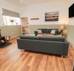A living room with two sofas a wood stove and a wall mounted television at The Bakery in Middleton near Belford