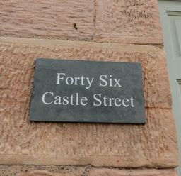 A stone wall with a sign showing Forty Six Castle Street at 46 Castle Street in Norham