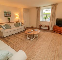 A living room with two sofas a round wooden coffee table a television on a wooden stand a small bench under a window and table lamps at 46 Castle Street in Norham