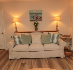 A beige sofa with cushions and a plant on a shelf with two lit lamps on the sides at 46 Castle Street in Norham