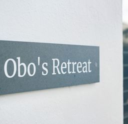 A close up of a sign reading Obos Retreat on a white wall at Obo's Retreat in St Minver near Rock
