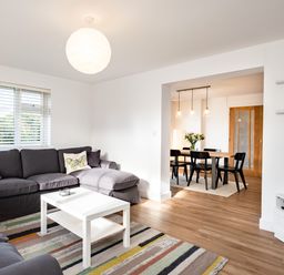 A living room with dark gray sofas a white coffee table a striped rug and a view of a dining area at Obos Retreat in St Minver near Rock