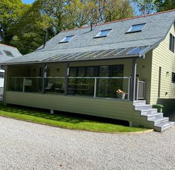 A modern house with a glass railing porch and steps on a gravel driveway surrounded by grass at Primrose Hellandbridge near Bodmin