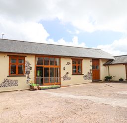 A courtyard with a barn building featuring wooden windows and doors at Quoit X Barn in Stoodleigh near Bampton