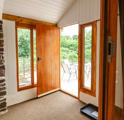 An entryway with a wooden door open to a patio with outdoor chairs and a table at Quoit X Barn in Stoodleigh near Bampton