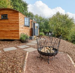 A wooden cabin with a fire pit and outdoor seating in a garden at Hideaway Cabin in Cadbury near Thorverton
