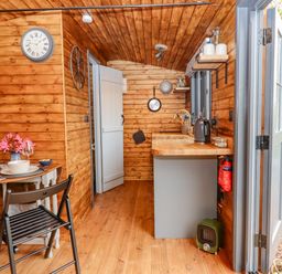 A small wooden kitchen and dining area with a table set for two and an open door leading outside at Hideaway Cabin in Cadbury near Thorverton
