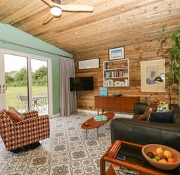 A living room with a patterned chair a black sofa wooden coffee table and a wooden cabinet with shelves at Lulu Logs Congresbury