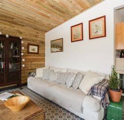 A living room with a white sofa with patterned cushions a wooden cabinet with books and ornaments a wooden coffee table with a bowl and a plant at Down the Rabbit Hole Brinsea near Congresbury