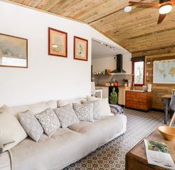 A living room with a beige sofa and patterned cushions next to a kitchen and dining area with wooden ceiling at Down the Rabbit Hole Brinsea near Congresbury