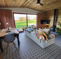A living room with a wooden dining table and chairs a white sofa with colorful blankets a wood stove and a decorated Christmas tree at Down the Rabbit Hole Brinsea near Congresbury