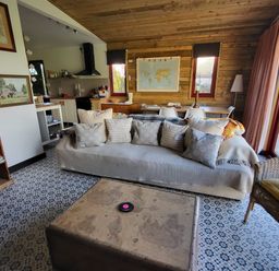 A living room with a sofa and cushions a coffee table a bookshelf and a kitchen area at Down the Rabbit Hole in Brinsea near Congresbury