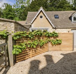 A stone house with a wooden gate and wooden fence with plants at The Hayloft in Sherston