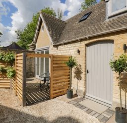 A stone cottage exterior with a small fenced patio and two potted plants at The Hayloft in Sherston