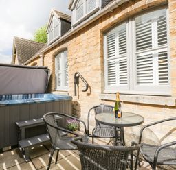 An outdoor patio with a hot tub table with a bottle and glasses and four chairs at The Coach House in Westonbirt near Tetbury