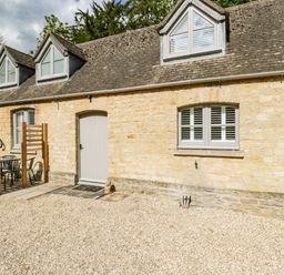 A stone cottage exterior with multiple dormer windows outdoor seating and a gravel area at The Coach House Westonbirt near Tetbury