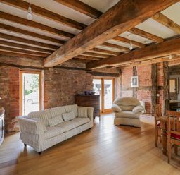 A living room with a striped sofa an armchair wooden dining table and exposed beams at Munderfield Mill in Munderfield near Bishops Frome