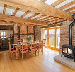 A dining room with a wooden table and six chairs near a wood burning stove at Munderfield Mill in Munderfield near Bishops Frome