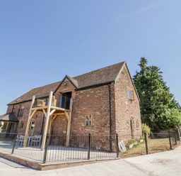 An exterior view of a brick building with a wooden balcony and metal railings at Munderfield Mill in Munderfield near Bishops Frome
