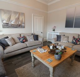 A living room with two beige sofas a wooden coffee table with cups and a plant and wall art at Spinnaker House in Scarborough