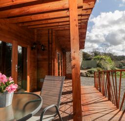 A wooden porch with a glass table and chair overlooking a garden at Bearscombe View in Modbury